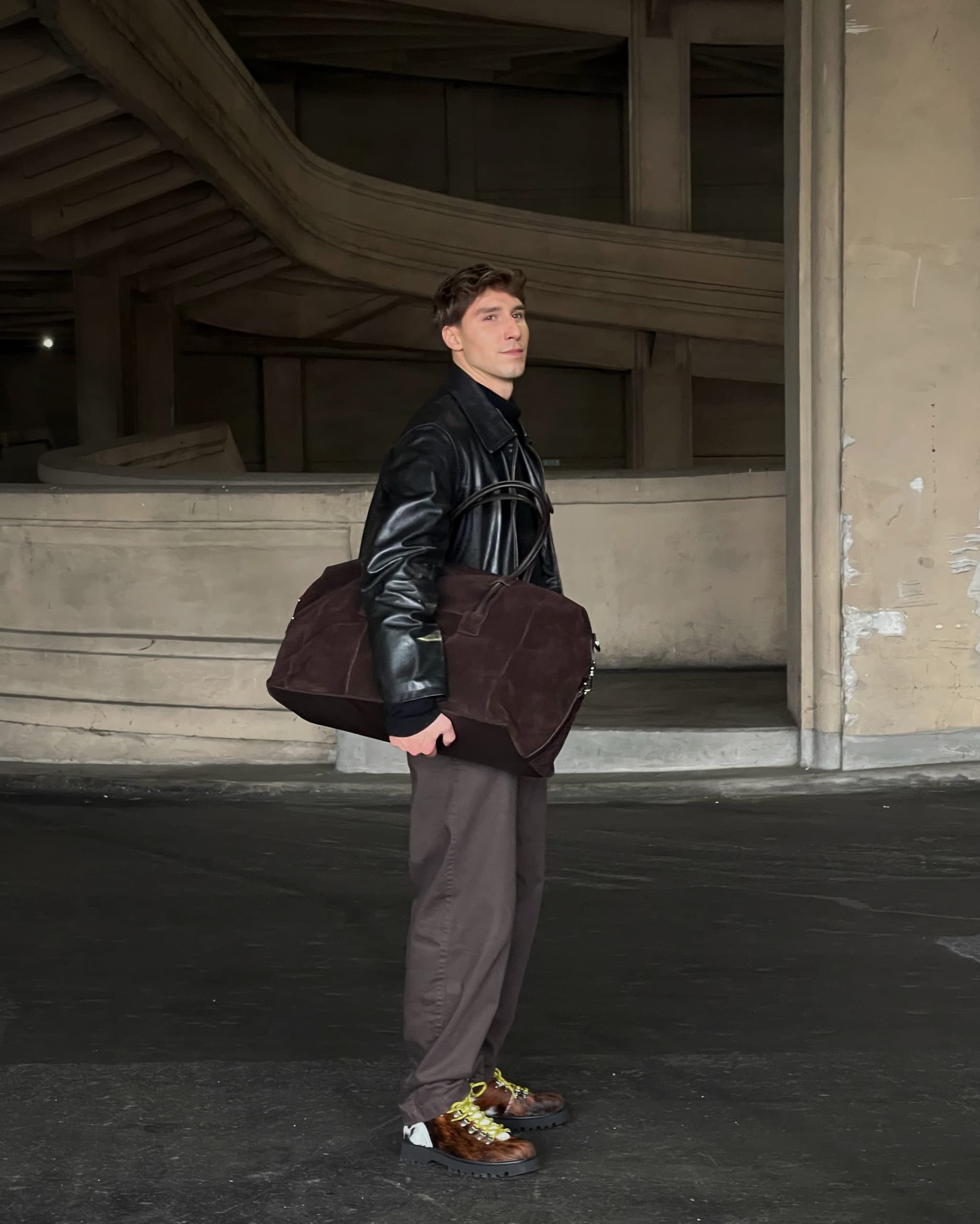 Man carrying a Kazar leather duffel bag in an architectural setting.