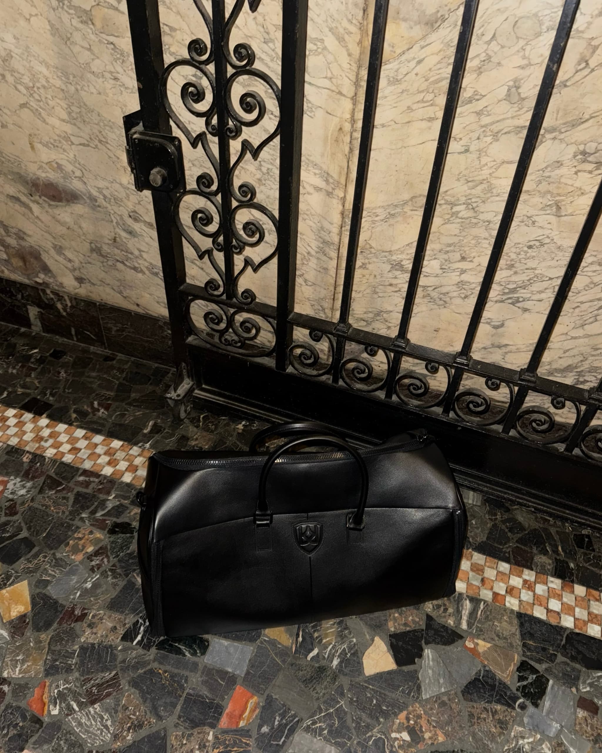Black Kazar duffel bag placed before an ornate wrought-iron gate.